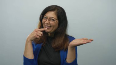 Mavi ceketli kadın gülümsüyor ve stüdyoda açık avuca işaret ediyor açık mavi arka planda; sıcak dostça bir davet.