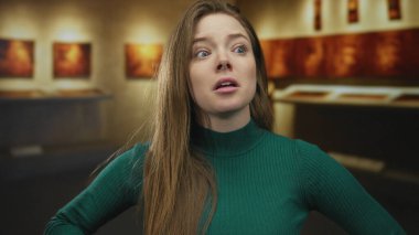 Modern müzedeki sanat eserlerini işaret eden ve kulağına dokunan kadın, merak yansıması.