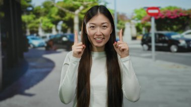 Şehir caddesinde ağaçlarla çevrili bir yerde gülümseyen, günlük beyaz elbiseler giyen ve gün boyunca sevinçle el kol hareketi yapan bir kadın..