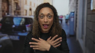 Genç kadın açık ağızlı ve caddede geniş gözleri ile yanakları tutar; sürpriz tepki an şaşkınlık.