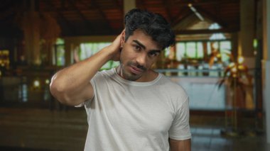 Beyaz gömlekli adam otel binasında eli boynu ve başı hafifçe eğik duruyor. Belirsizlik..