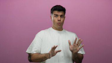 Genç adam canlı pembe bir arka plana karşı şaşkınlığını dile getiriyor. Elleri havada, günlük beyaz bir gömlek giyiyor. Duygusal ve anlamlı bir anın altını çiziyor..