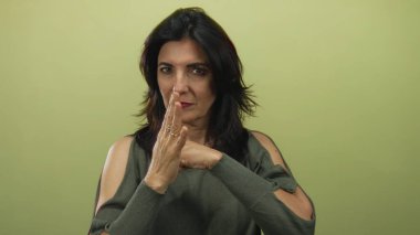 Orta yaşlı bir kadın stüdyoda kamerayı doğrudan zeytin yeşili duvara doğrultuyor..