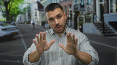Genç İspanyol adam, işlek şehir caddesinde geri dönüşüm konteynırının önünde ellerini açık gösterdi..