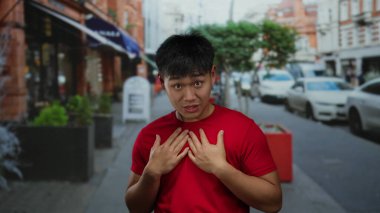 Şehir caddesinde kırmızı tişört giyen genç adam arka planda arabalar ve binalarla açık havada duygularını ifade ediyor..