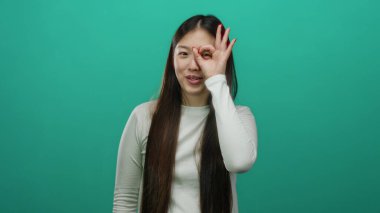 Yeşil arka planda poz veren kadın el hareketi yapıyor. Gözlüğü parmaklarıyla temsil ediyor. Ayrı bir ortamda neşe ve dışa dönük iletişimi vurguluyor..