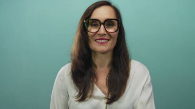 Dudakları üzerinde parmaklarıyla sessizlik gösteren, gözlüklü, izole edilmiş mavi duvar arkaplanı olan bir kadın..