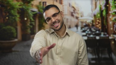 Gözlüklü genç İspanyol adam, sokakta el sıkışarak gülümsüyor, arkadaşlığı selamlıyor..