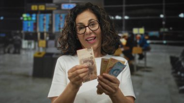 Havaalanı terminalinde Meksika pesolarını sayan gülümseyen bir kadın, seyahat finans kavramını mutluluk ve beklentiyle taşıyor..