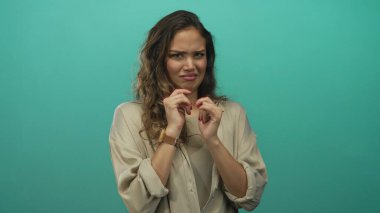 Şüpheli ifadeli bir kadın, yeşil arka planda, bej gömlek giyiyor, şüphe ve hoşnutsuzluğu ifade ediyor, İspanyol, genç, eller havada, ciddi, uzun saçlı..