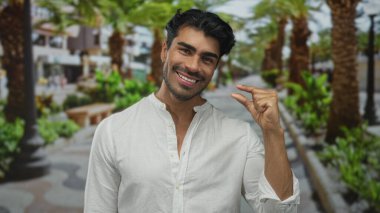 Adam, palmiye ağaçları ve bankları olan yeşil bir parkta başparmak ve işaret parmağı çimdikler; hassasiyet ölçümü.