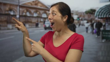 İspanyol kadın kırmızı gömlek giyerken sokak binasını işaret ediyor ve göz kırpıyor..