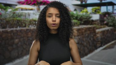 Genç İspanyol kadın taştan duvarın yanında açık avuçlar ve gün ışığında çiçek açan çalılar gösteriyor..