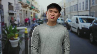 Sokaktaki genç adam, arka planda trafik ve yayaların görüldüğü hareketli bir şehir sahnesinde kargaşa yaratıyor.