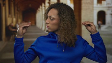 Mavi kapüşonlu, tarihi caddede konuşmalı el hareketi yapan bir kadın..