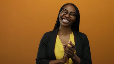 Sarı bluz ve gözlük takmış, turuncu arka planda el çırpan kadın, izole edilmiş sıcak bir ortam ve canlı bir ortam ile neşeli bir ifade sergiliyor..