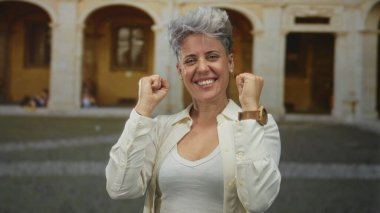 Beyaz kolsuz tişörtlü bir kadın tarihi kasaba binasındaki kaldırım taşı caddesinde kısa gri saçlarını savuruyor..