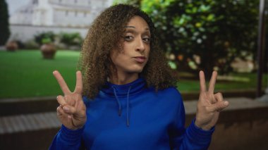 Transseksüel İspanyol kadın, bir binanın dışındaki şehir sokağında elleri ile çifte barış işareti gösteriyor..