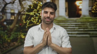 Hispanik adam tarihi binanın ön cephesinin önünde el hareketi yapıyor; şükran duygusu barış umudu saygı.