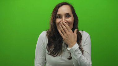 Ağzı açık gezen bir kadın canlı yeşil bir arka plana karşı sürpriz bir jest yaparak beyaz bir gömlek giyerek çerçevede izole edilmiş duygularını ve kişiliğini ifade ediyor..