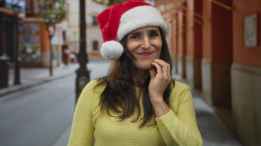 Latin kökenli genç bir kadın, şehir caddesinde diş ağrısı için elleriyle yanağa dokunuyor; diş ağrısı rahatsızlığı.