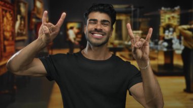 Erkekler sanat galerilerinde geniş bir gülümseme ile heykeller ve tablolar arasında kaya boynuzları hareketi yapar; sevinç kutlaması.