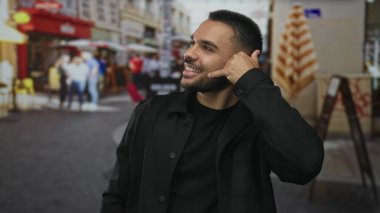 İnsan, meşgul caddede eli ve gülen yüzüyle telefon jesti yapıyor. Görünürde bulanık yayalar, mutluluk....