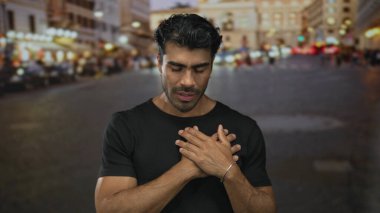 Alacakaranlıkta kalabalık bir şehir sokağının önünde siyah tişört giyen İspanyol bir adam..