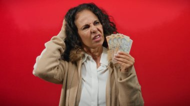 Kadın, Romanya 'nın parasını elinde tutan kırmızı bir zemine karşı belirsiz bir ifadeyle, finans ve duygu temalarını yakalıyor.