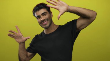 Sarı stüdyoda elleri ve gülümseyen yüzü olan, enerjik duruşu olan adam çerçeveleme sahnesi; neşe yaratıcılığı vizyonu.