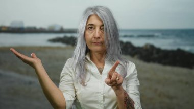 Yaşlı bir kadın, kumsalda bir şey sunarken, serin bir açık deniz sahnesini çekerken, parmağıyla işaret ediyor..