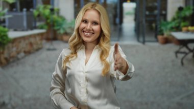 Şehrin arka planında el sıkışarak gülümseyen bir kadın, açık havada beyaz gömlekli sarışın genç bir kadın şehir yeşili ve dost canlısı atmosferle çevrili..