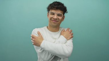 Gözlüklü ve beyaz süveter giyen İspanyol genç adam stüdyoda omuzlarına sarılıyor..