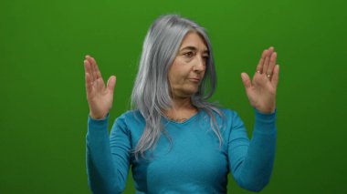 Büyük beden jest yapan, yeşil duvarlara yaslanmış, mavi bir süveter giyen, dışlanmış bir ortamda ifade ve duygu aktaran yaşlı bir kadın..