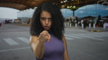 Ciddi ifadeleri olan genç İspanyol kadın, havaalanının kalkış terminali binasında kamerayı işaret ediyor..