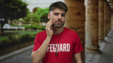 Can kurtaran ıslık çalan ve kırmızı gömlekli adam binadaki taş sütunlu yeşil park yolunun yanındaki yanağa dokunuyor..