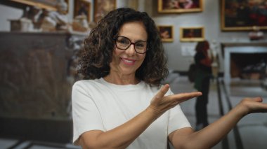 Orta yaşlı İspanyol kadın, açık jest müzesi sergi salonunu uzattı; davet olumlu nişan.