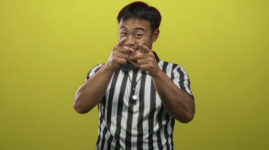Sarı stüdyoda, çizgili tişört giyen genç Çinli hakem kamerayı işaret ediyor..