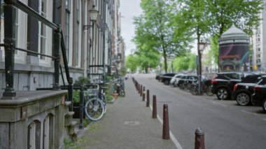 Bisikletler, arabalar ve tarihi mimarinin yer aldığı büyüleyici Amsterdam caddesi manzarası. Bulanık, yeşil ağaçlar ve bulutlu gökyüzü..