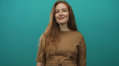 Stüdyo ortamında uzun kızıl saçlar ve açık renk çillerle gülümseyen bir kadın..