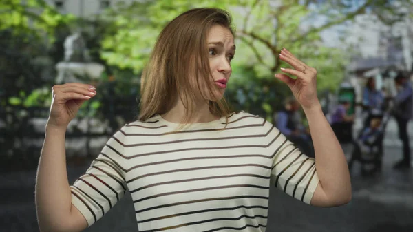 Güneşli bir günde yeşil bir parkta çizgili bir jest giyen genç bir kadın, coşkulu bir iletişim..