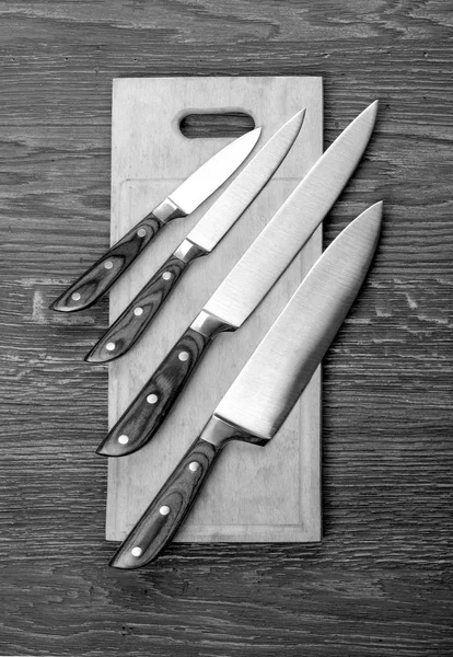 Set of kitchen knifes on wooden cutting board on old wooden table