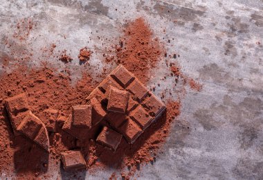 Kırık çikolata parçaları ve tahta arka planda kakao tozu.
