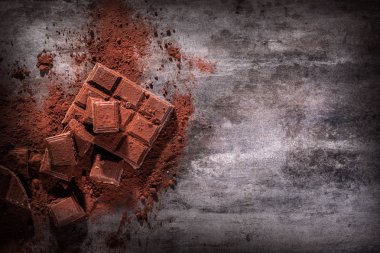 Kırık çikolata parçaları ve tahta arka planda kakao tozu.