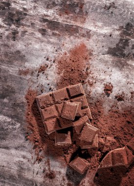 Kırık çikolata parçaları ve tahta arka planda kakao tozu.