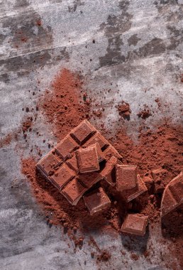 Kırık çikolata parçaları ve tahta arka planda kakao tozu.