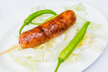 Yeşil biber ile beyaz bir tabak içinde domuz sosisi.