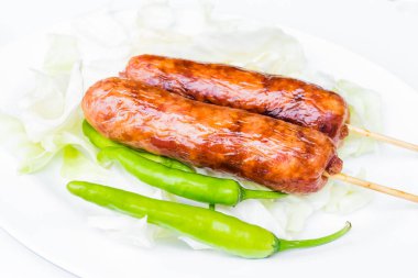 Yeşil biber ile beyaz bir tabak içinde domuz sosisi.