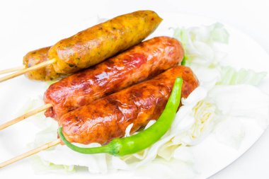 Yeşil biber ile beyaz bir tabak içinde domuz sosisi.