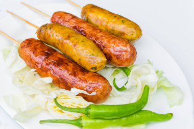 Yeşil biber ile beyaz bir tabak içinde domuz sosisi.